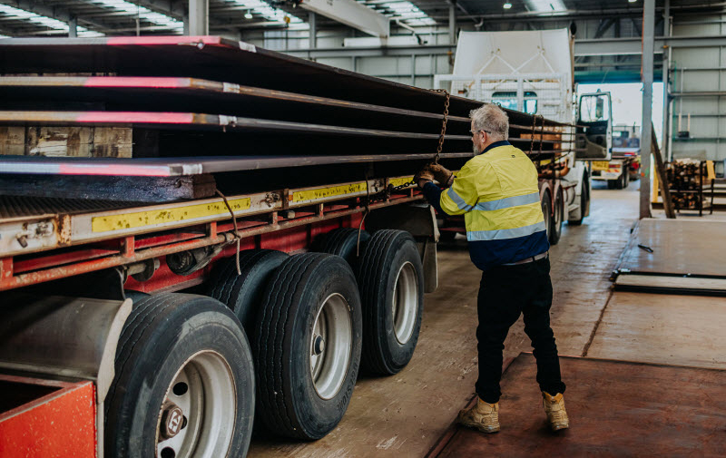 Southern Steel WA Delivering what no one else can Employee wearing a uniform putting a chain for the steel products loaded on the truck